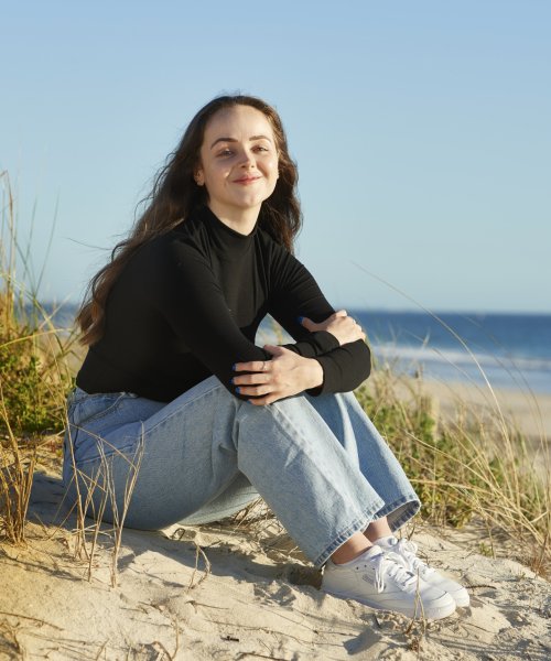 A smiling young woman sits on the beach during the morning