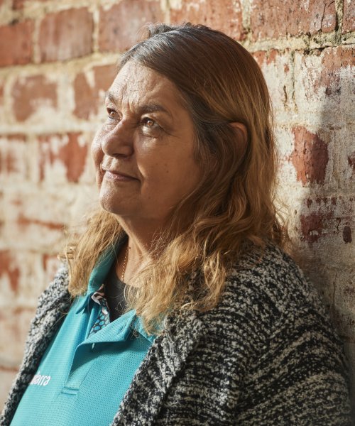 An Indigenous Australian woman looks up while leaning against a wall