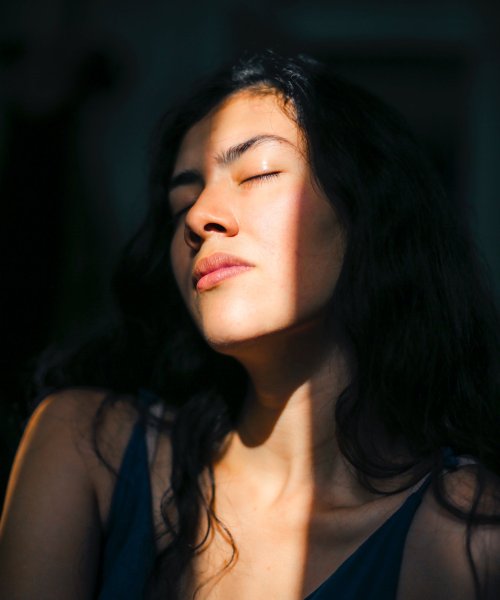 A young woman closes her eyes against the sunlight that seeps into a dark room