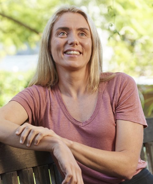 A Caucasian woman smiles while leaning back on an outdoor bench