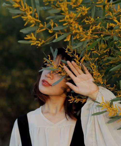 A young woman hides behind the branches and blossoms of a young tree