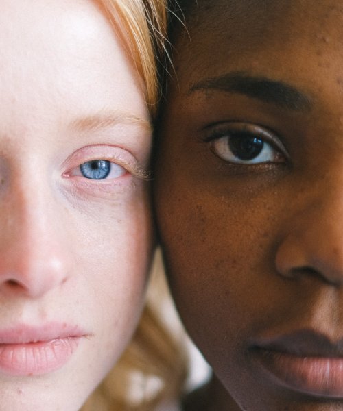 A Caucasian and African woman stand with their faces side by side